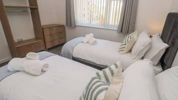 Een hotelkamer met twee bedden, een houten plank, een raam met zonwering en een nachtkastje.