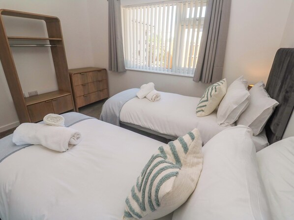 A hotel room with two beds, a wooden shelf, a window with blinds, and a bedside table.