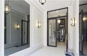 A hallway with a glass door leading to a room, a light fixture on the wall, and a mirror reflecting the interior. - EXCEPTIONAL 200 M² PENTHOUSE, JUST A ONE-MINUTE WALK FROM THE ICONIC CROISETTE (Cannes)
