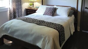 Una camera da letto con un letto, un ventilatore a soffitto, un comodino con una lampada, un'opera d'arte a parete e una porta.