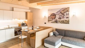 A modern kitchen with white cabinets, a dining area with a gray sofa, and a wall-mounted picture. - Elbetina Penthouse, in the center of Campitello di Fassa with a panoramic view (Campitello di Fassa)