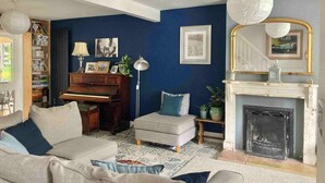 Una sala de estar con un piano, una chimenea, una escalera y una estantería.
