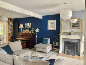 Ein Wohnzimmer mit Klavier, Kamin, Treppe und Bücherregal.