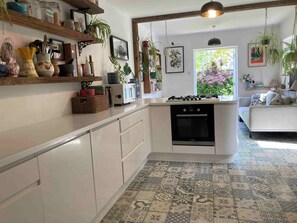 A kitchen with a central island, a stove, and a sink. There are shelves with jars and plants, and a window with a view of greenery. - Cambridge Center - Riverside - On a no-through road leading to the River Cam (Cambridge)