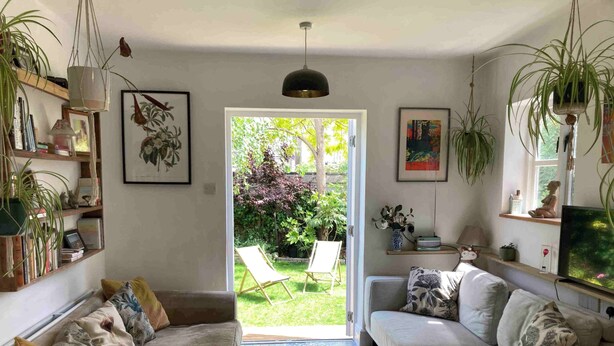 A living room with a sofa, a coffee table, a TV, and a kitchen area with a stove. There is a door leading to a garden. - Cambridge Center - Riverside - On a no-through road leading to the River Cam (Cambridge)