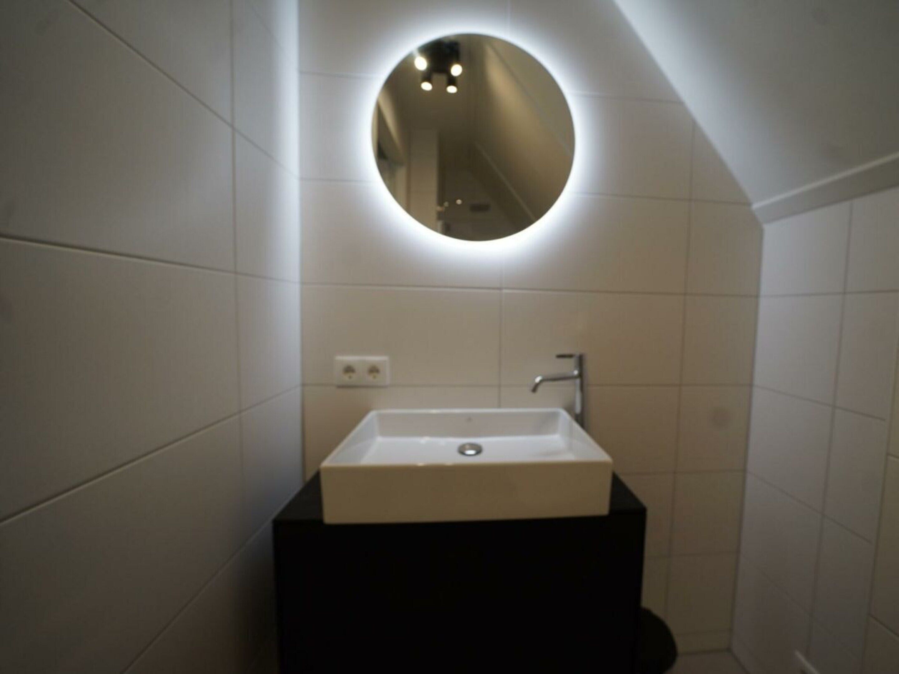 A bathroom with a rectangular sink, a mirror, and a wall-mounted light fixture.