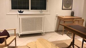 Een kamer met raam, radiator, houten meubels en een ingelijst kunstwerk aan de muur.