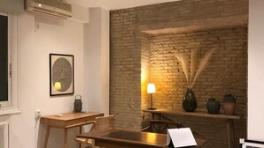 Een kamer met een bakstenen muur, een houten tafel, stoelen, een lamp en een lijst met een afbeelding.