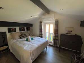 Une chambre à coucher avec un lit, une commode, une fenêtre avec des rideaux et un ventilateur de plafond.