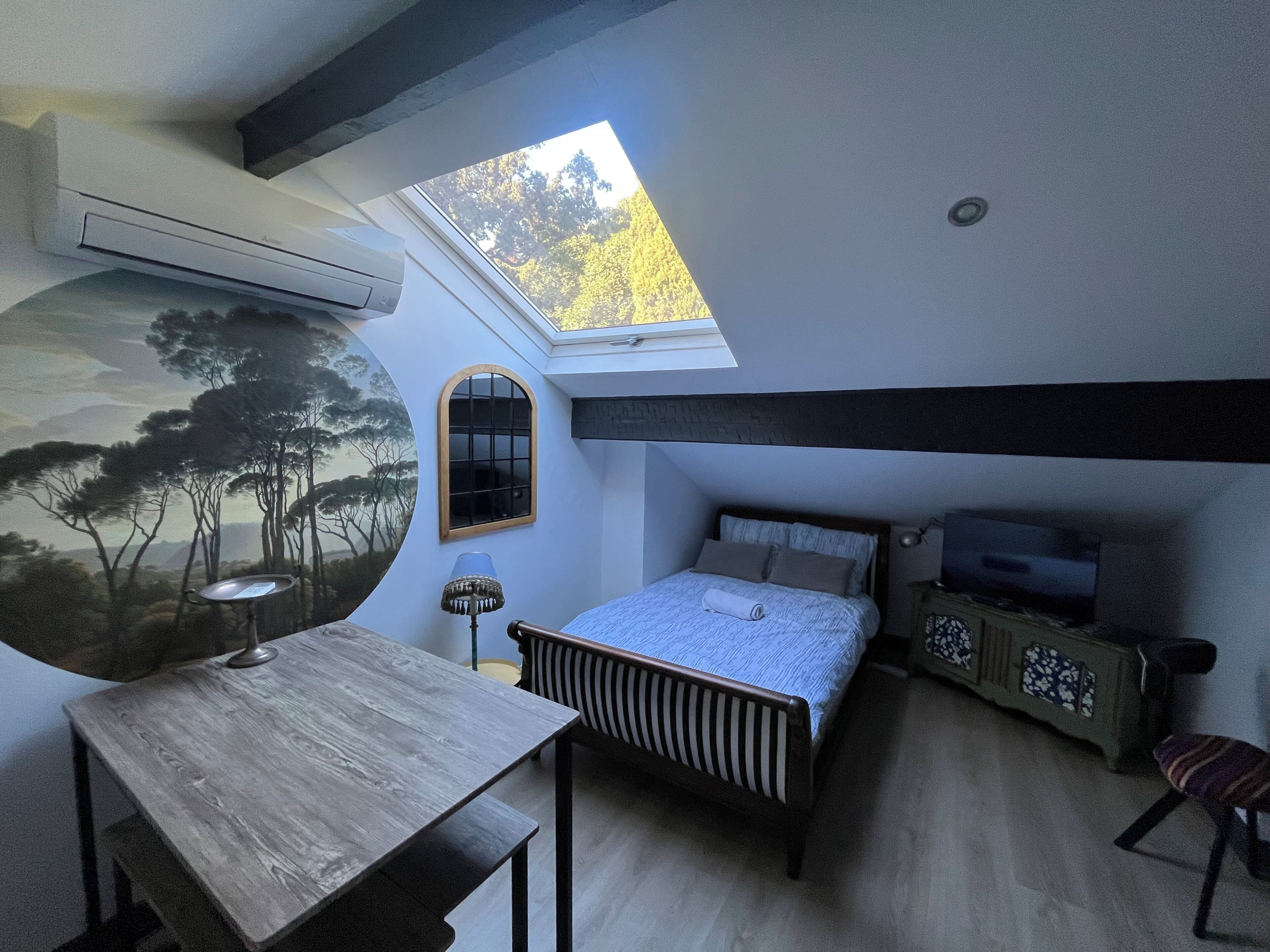 Ein Schlafzimmer mit Dachfenster, einem Bett, einem Schreibtisch, einem Sessel und einem Fernseher.