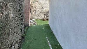 A narrow alleyway with a brick archway, a grassy area, and a white wall with a window and a light fixture. - NEMO Apartment by Ateya - L'Estaque (Marseille)