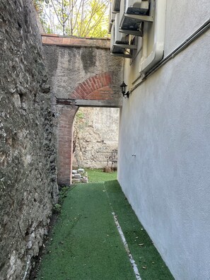 A narrow alleyway with a brick archway, a grassy area, and a white wall with a window and a light fixture. - NEMO Apartment by Ateya - L'Estaque (Marseille)