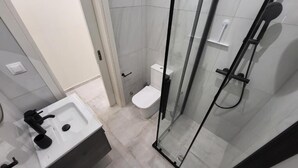 Un baño con ducha de vidrio, lavamanos blanco y un inodoro.