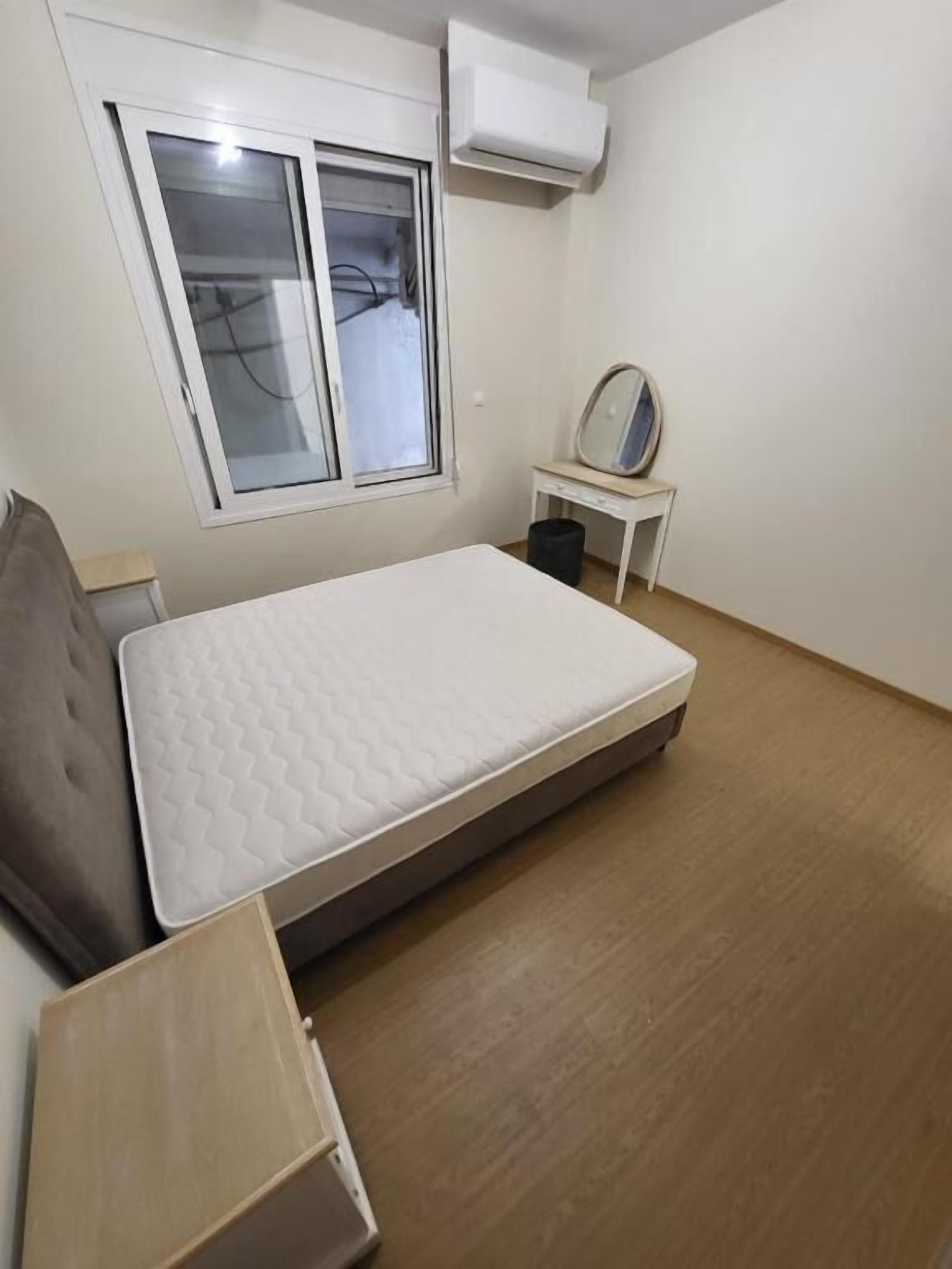 A bedroom with a bed, a window, a small table with a mirror, and an air conditioning unit.