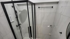 Un baño con cabina de ducha de vidrio, inodoro y lavamanos con espejo.