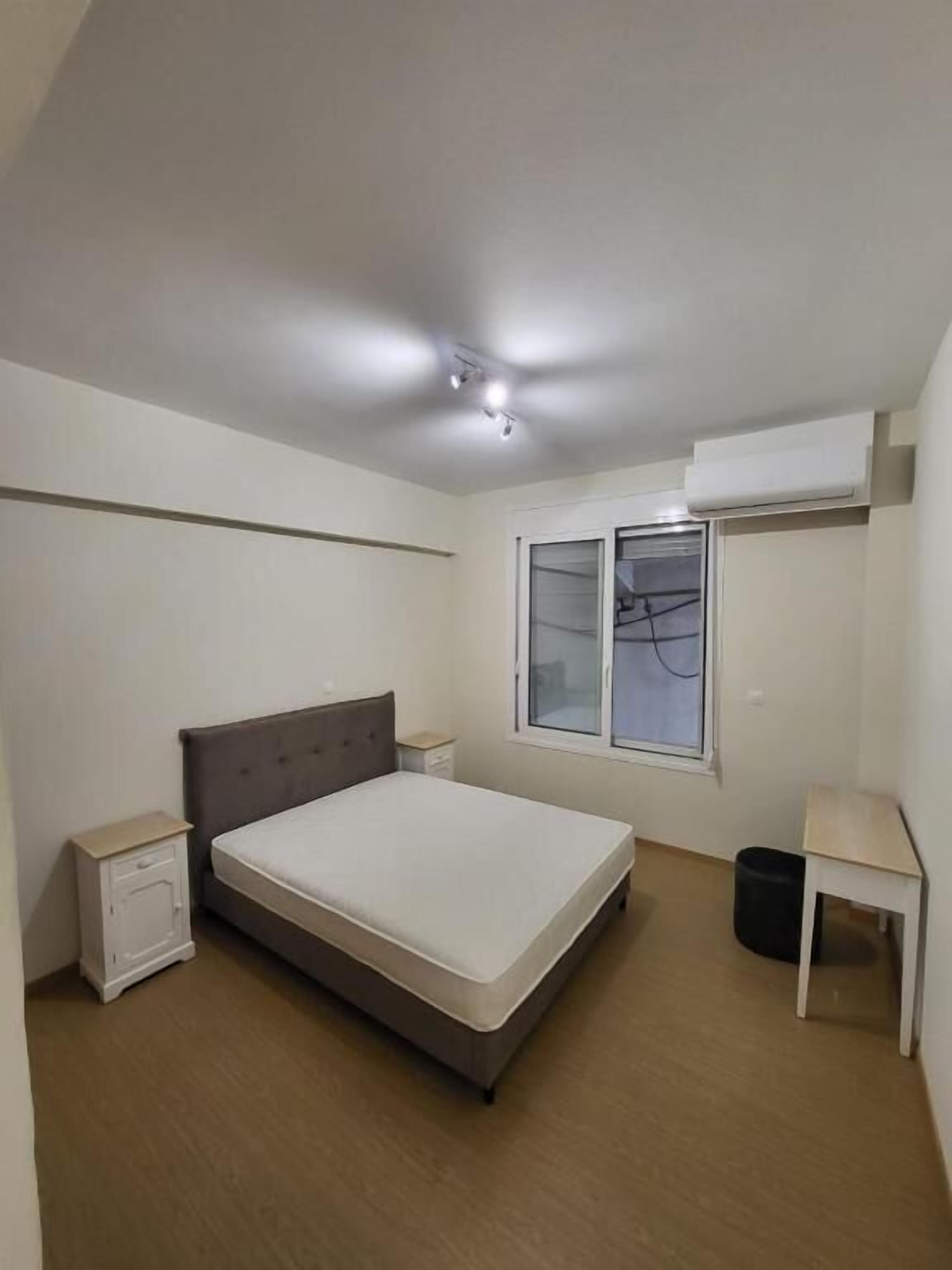 Une chambre à coucher comprenant un lit, des tables de chevet, une fenêtre et un appareil de climatisation.