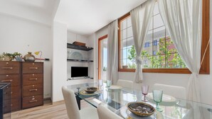 A modern kitchen with a glass dining table, white chairs, and a view of the outside through large windows.