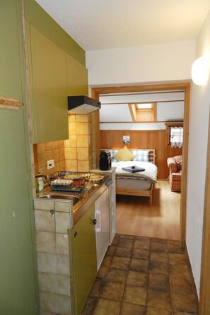 A compact kitchen with a sink, stove, and a dining area with a bed and a chair. - Studio Oehrli Studio, Dusche oder Bad, WC 2-Bettwohnung by Interhome (Gstaad)