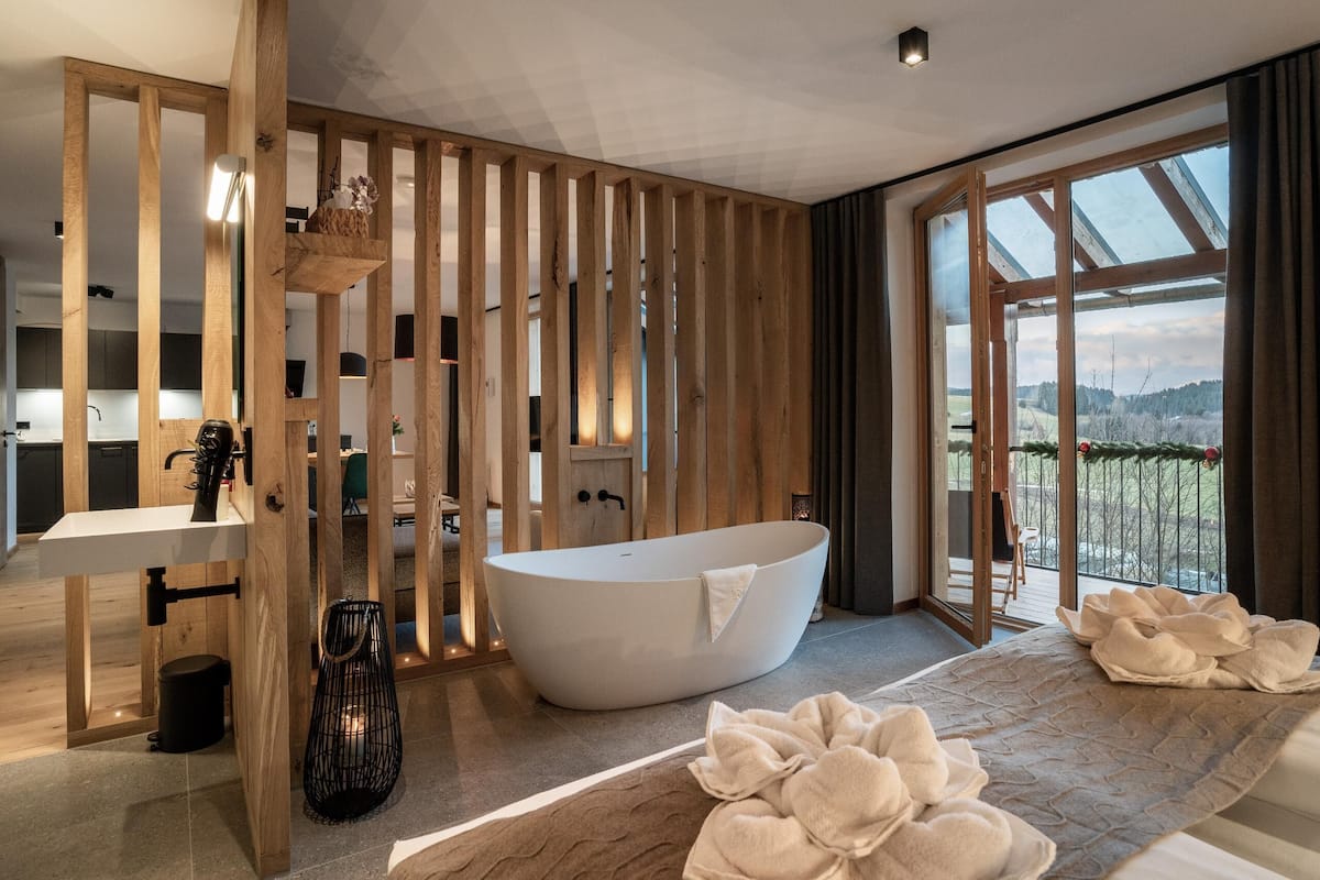 A modern bathroom with a freestanding bathtub, a wooden partition, and a view of the outdoors.
