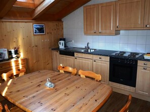 A wooden interior with a dining table, chairs, a kitchen area with a stove, sink, and cabinets. - Jacqueline 22 Appartement/Fewo, Dusche oder Bad, WC 5-Bettwohnung by Interhome (Gstaad)
