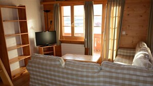 Een houten interieur met een bank, een televisie op een meubel en een raam met gordijnen.