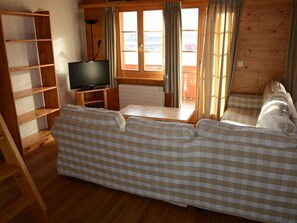 Ein Holzinnenraum mit einer Couch, einem Fernseher auf einem Schrank und einem Fenster mit Vorhängen.