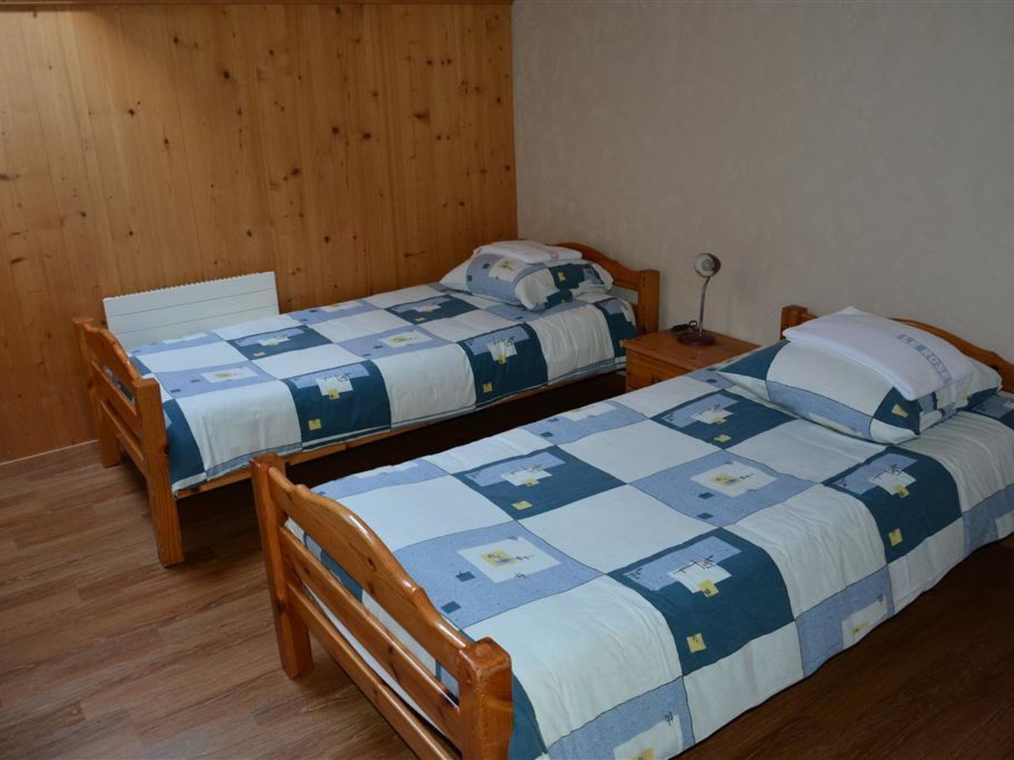 Een kamer met twee houten bedden met bijpassend beddengoed, een nachtkastje van hout en een wandlamp.