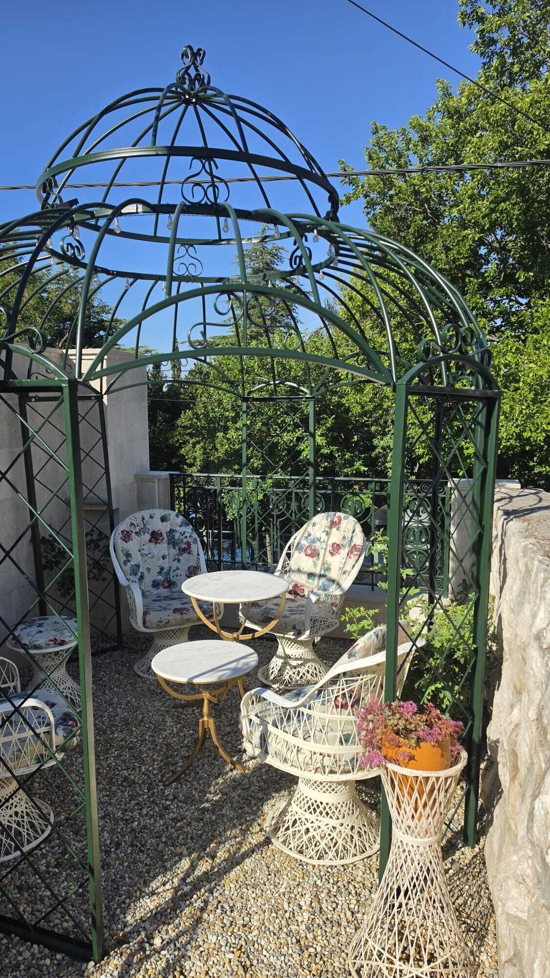 A garden gazebo with white wicker furniture and a decorative metal roof.