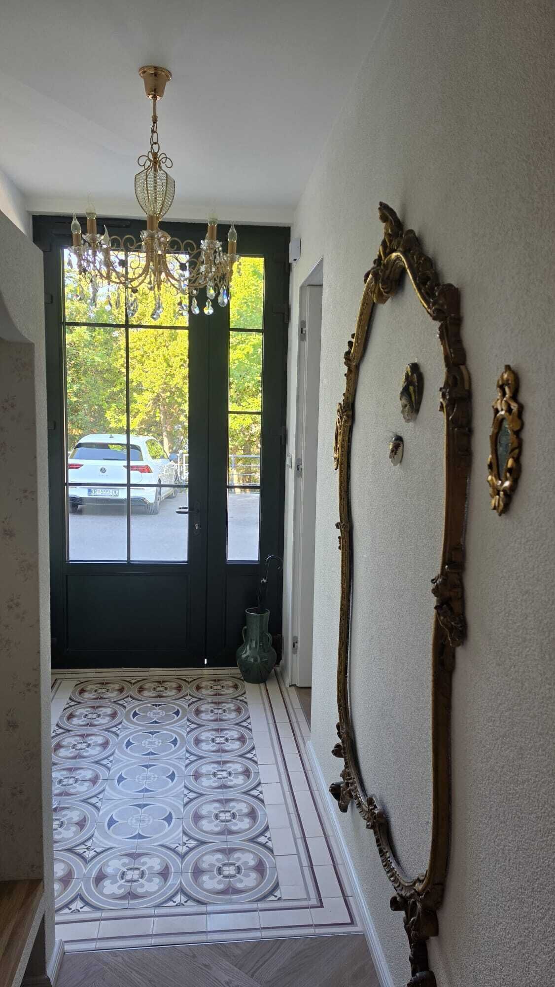 A hallway with a chandelier, a large ornate mirror, and a patterned floor.
