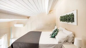 Ein Schlafzimmer mit einem Bett, Kissen, einem Nachttisch, einer Lampe und einer an der Wand befestigten Pflanze.
