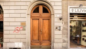 Eine Holztür mit Metallbeschlägen, ein kleiner Lüftungsschlitz darunter und ein Geschäft mit Schaufenster zur Rechten.