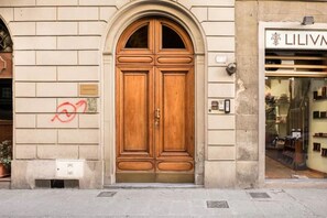 A wooden double door with a metal handle, a small vent below it, and a shop with a glass window to the right. - Stylish Florence Apartment Steps from the Duomo (Firenze)
