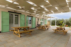 Een overdekt buitengebied met picknicktafels, groene deuren en een pergola.