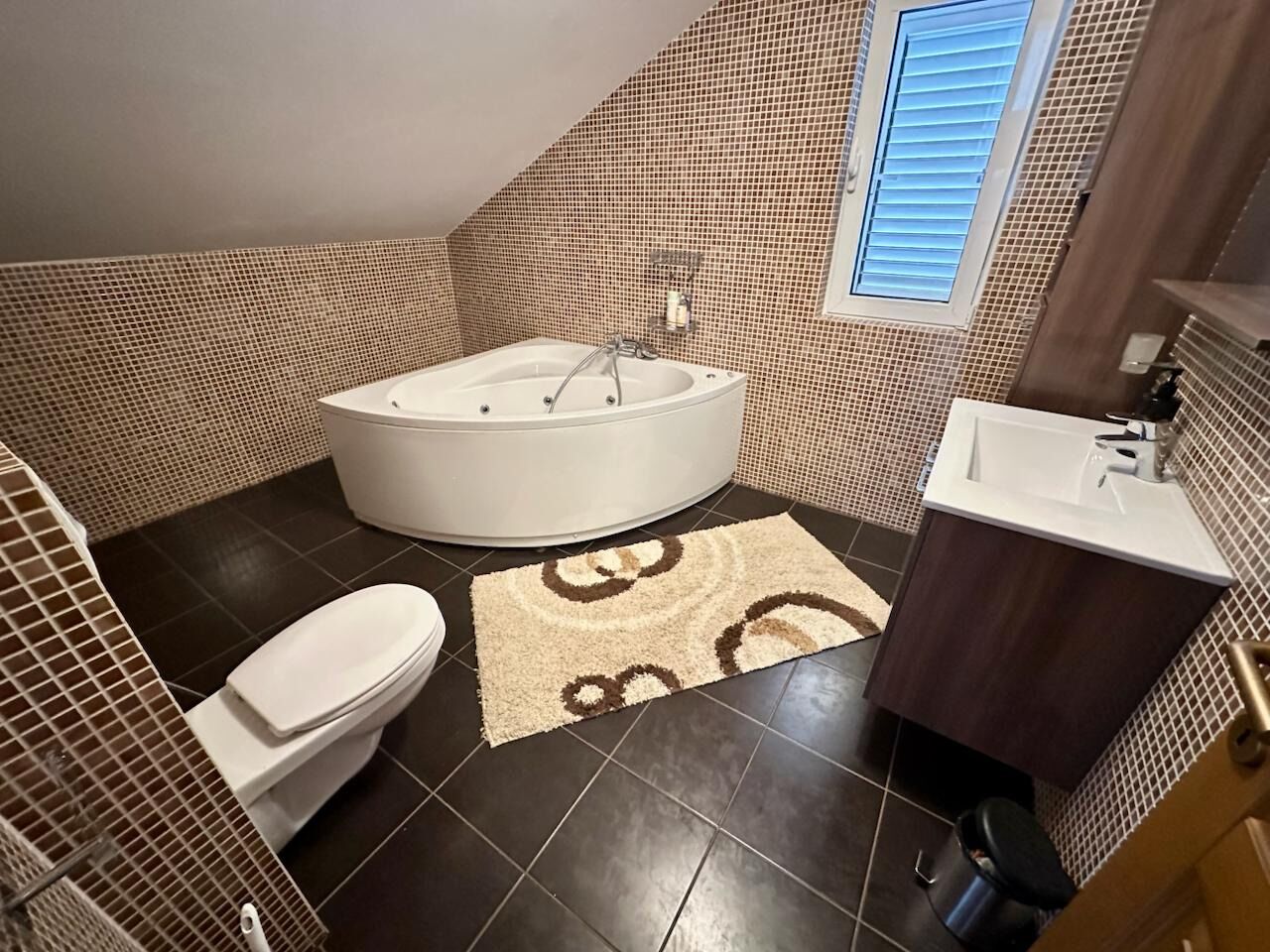 Een badkamer met bad, toilet en wastafel, met betegelde wanden en een vloerkleed met patroon.