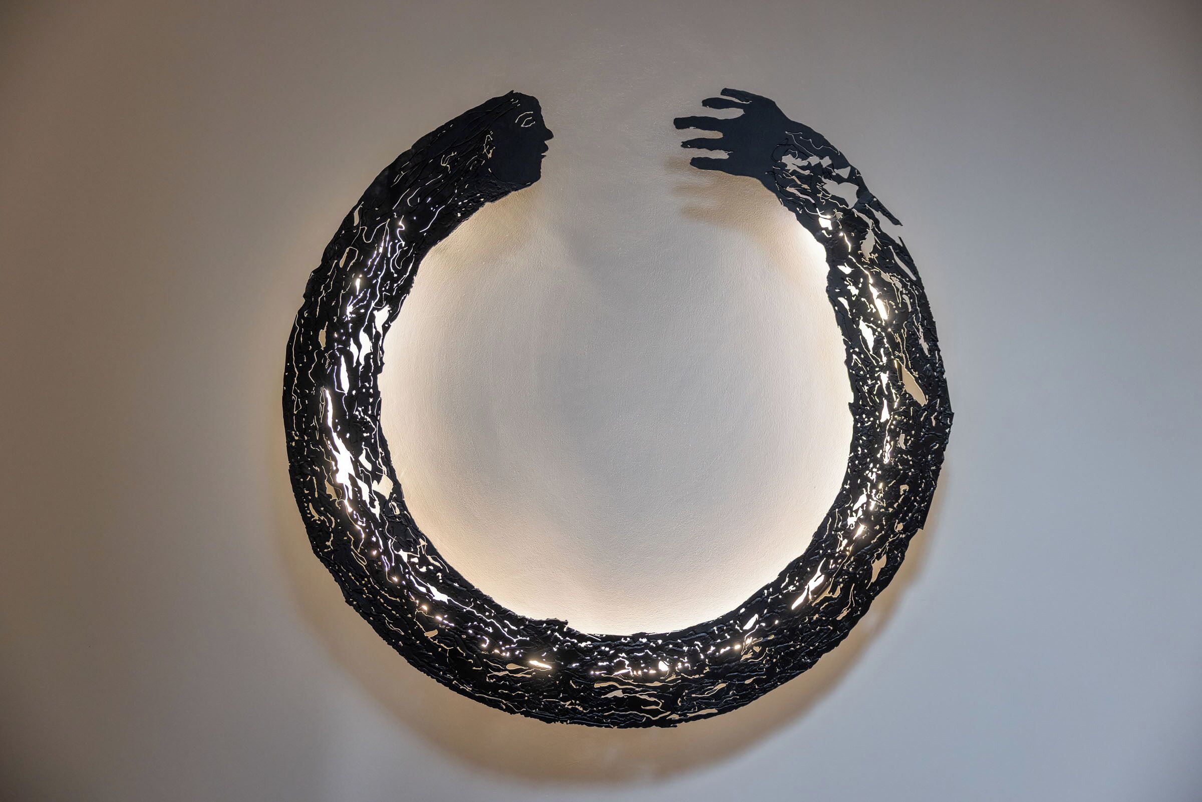 Una escultura negra y texturizada sobre una pared lisa.