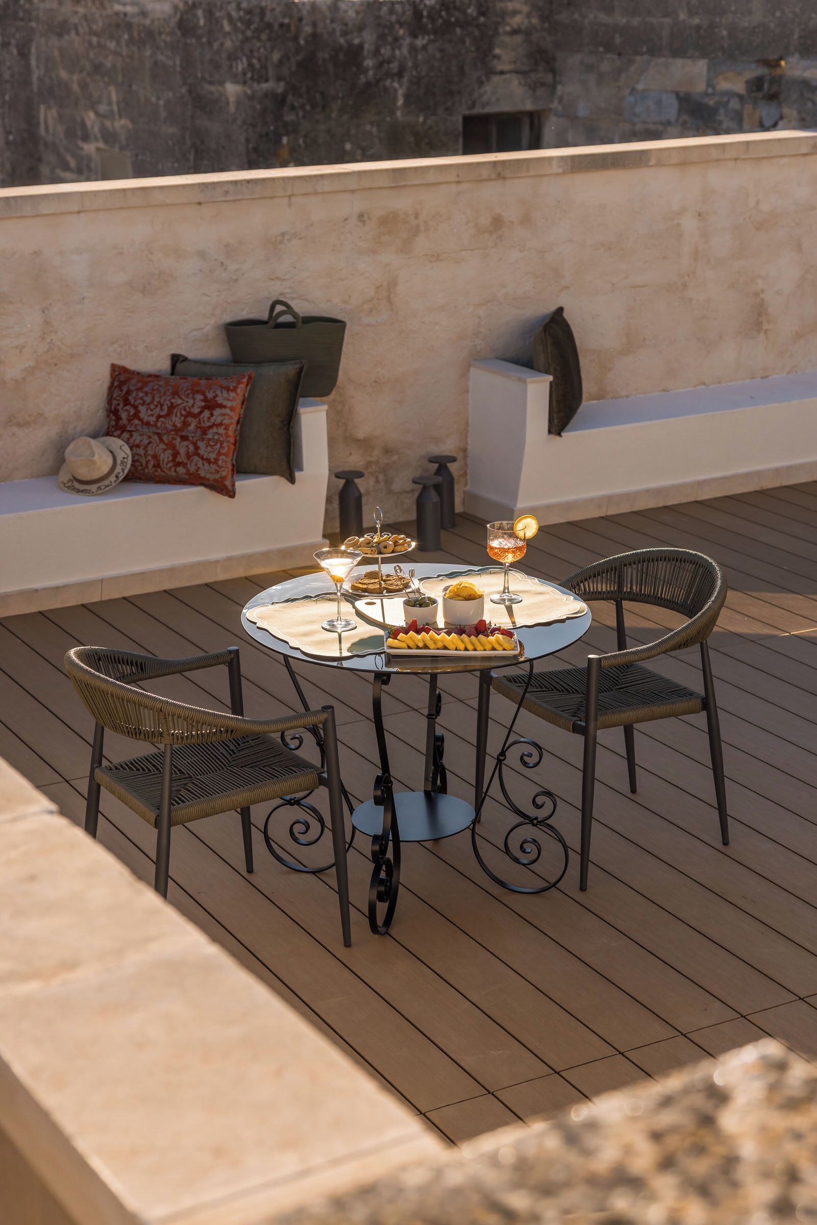 A round table with chairs on a wooden deck, a bottle of wine, and a glass of wine.