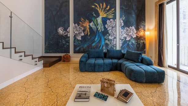 Un salon moderne avec un canapé d’angle, une table basse sur laquelle sont posés des livres et un grand tableau représentant un paon accroché au mur.