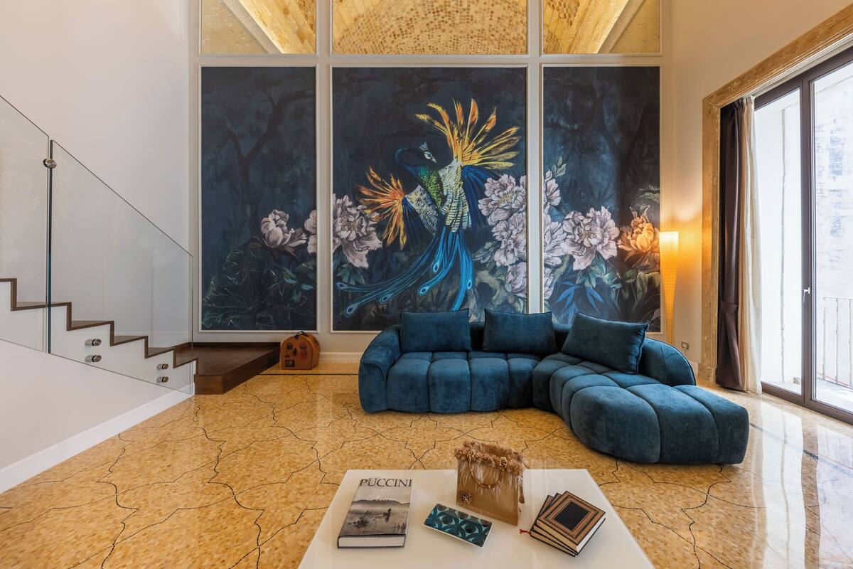 Uma sala de estar moderna com um sofá seccional, uma mesa de centro com livros e uma grande pintura de pavão na parede.