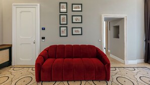 Un canapé rouge dans une pièce avec une porte blanche, un mur de couleur claire et des tableaux encadrés.
