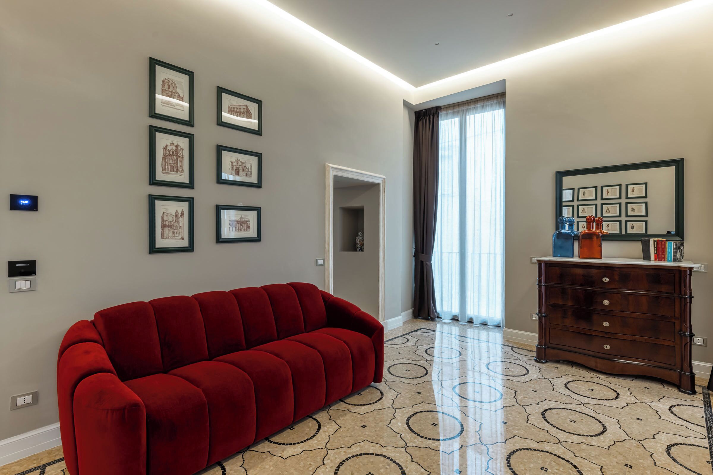 Una sala de estar moderna con un sofá rojo, un aparador de madera y obras de arte enmarcadas en las paredes.