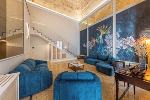 A modern living room with a staircase, blue sofas, a dining table, and a large painting. - Palazzo De'Belli Suites & Rooftop (Lecce)