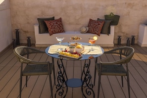 A round table with a white tablecloth, two wicker chairs, a sofa with patterned cushions, and a tray with food and drinks. - Palazzo De'Belli Suites & Rooftop (Lecce)