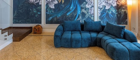 A modern living room with a blue sectional sofa, a white coffee table with books and a decorative item, and a large window with a mural of a peacock.