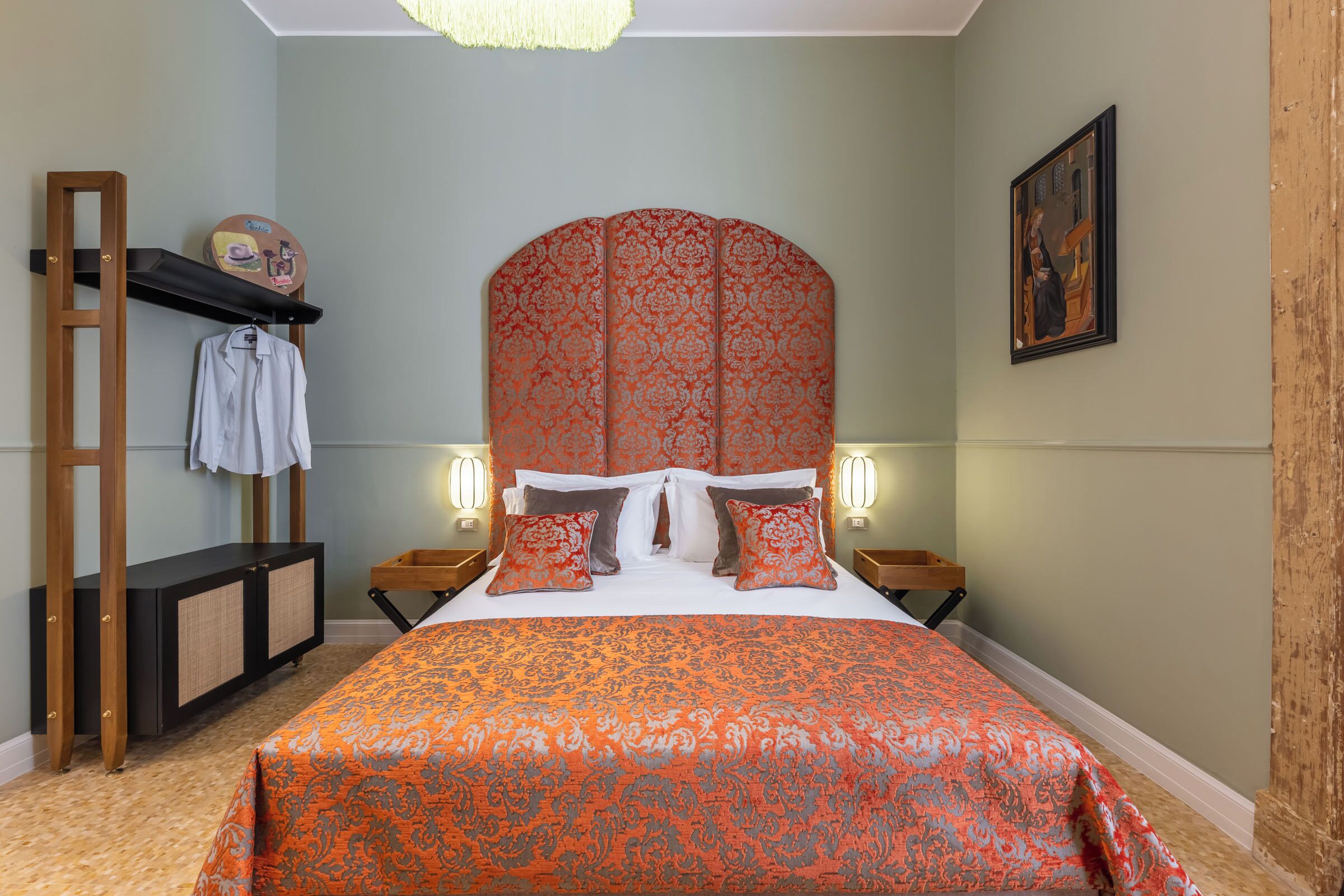 A bedroom with a large bed, a wooden headboard, a nightstand, a shelf with a towel, and a wall-mounted picture.