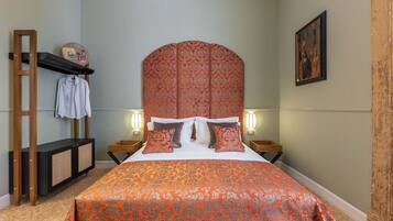 A bedroom with a large bed, a wooden headboard, a nightstand, a shelf with a towel, and a wall-mounted picture.