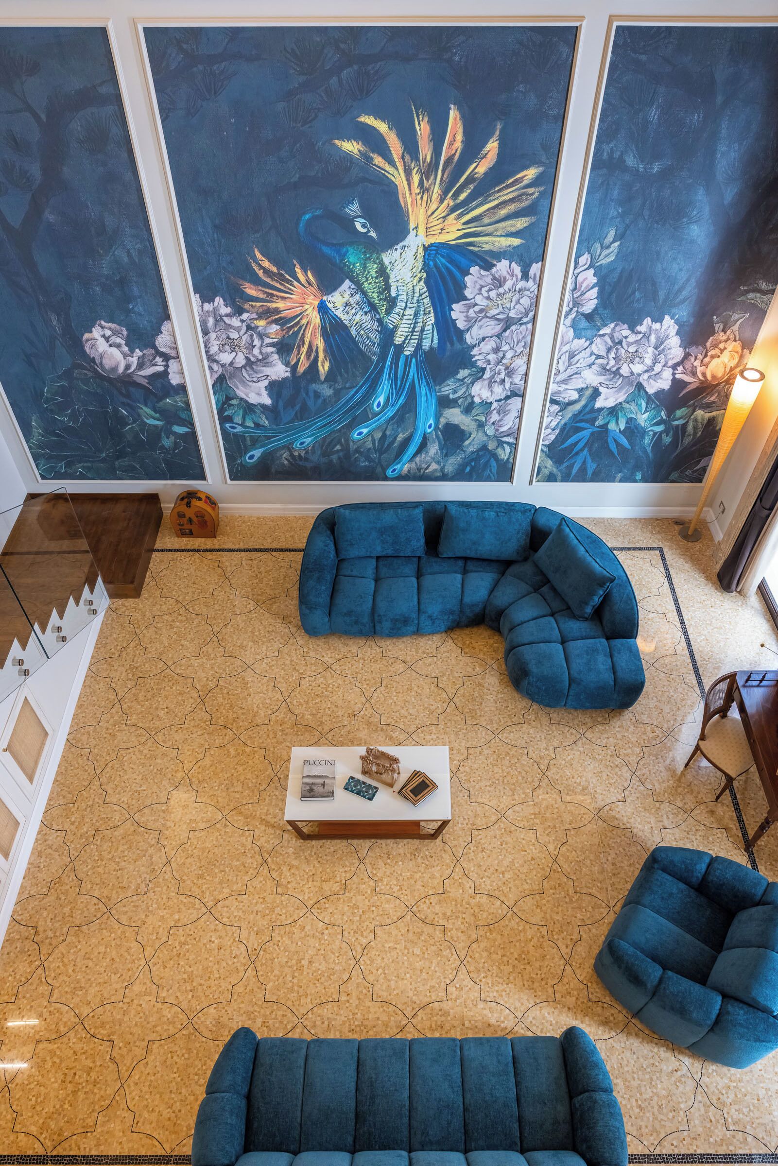 Una habitación con un cuadro grande de un pavo real, un sofá seccional azul, una mesa de centro y un suelo estampado.
