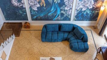 Una habitación con un cuadro grande de un pavo real, un sofá seccional azul, una mesa de centro y un suelo estampado.