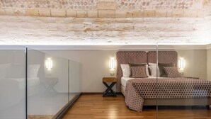 Une chambre avec un plafond en briques, un lit avec une literie à motifs, des lampes de chevet et une cloison en verre.
