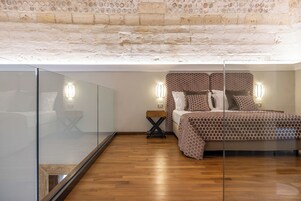 Un dormitorio con techo de ladrillo, una cama con ropa de cama estampada, lámparas de noche y un separador de vidrio.