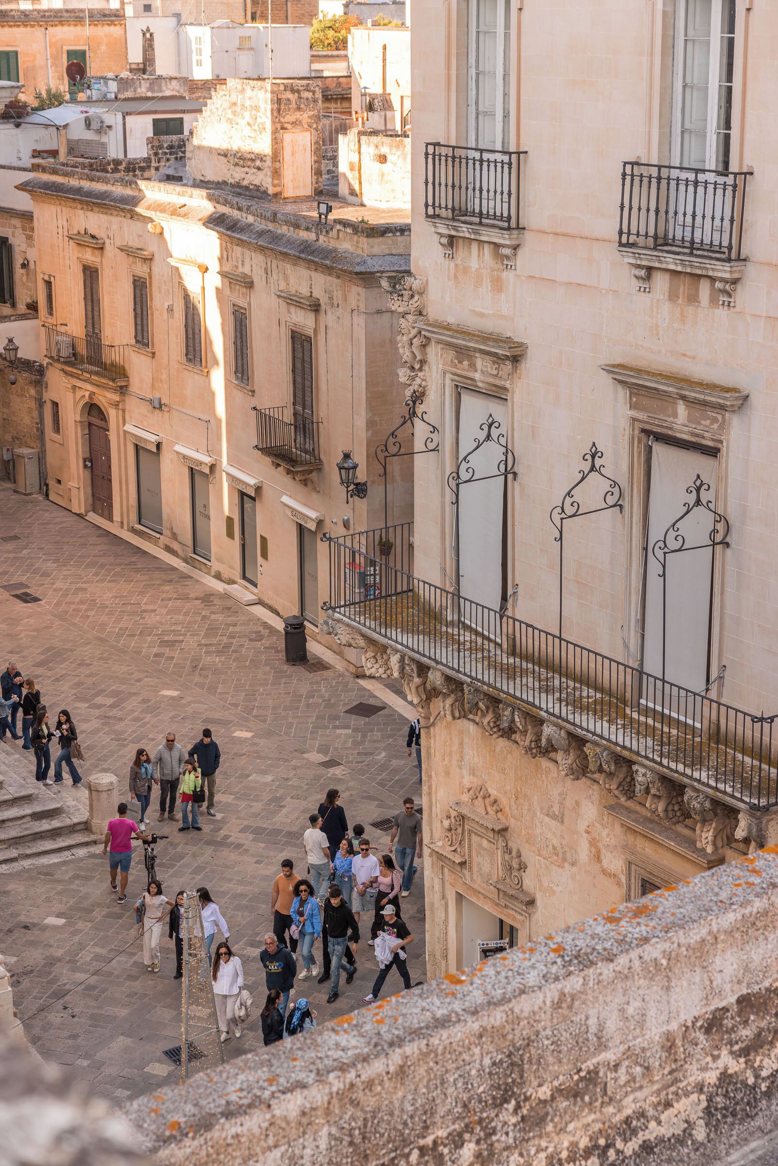 Una calle urbana con edificios históricos, una zona empedrada y una barandilla con vista a la calle.